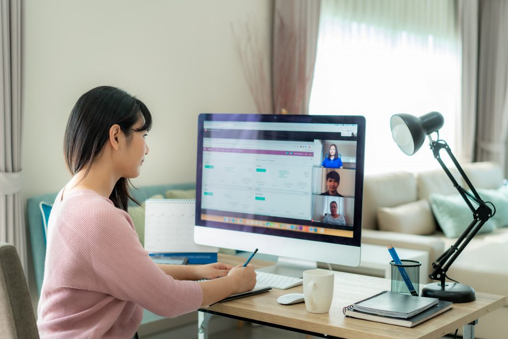 Back view of Asian business woman talking to her colleagues about plan in video conference. Multiethnic business team using computer for a online meeting in video call. Group of people smart working from home.