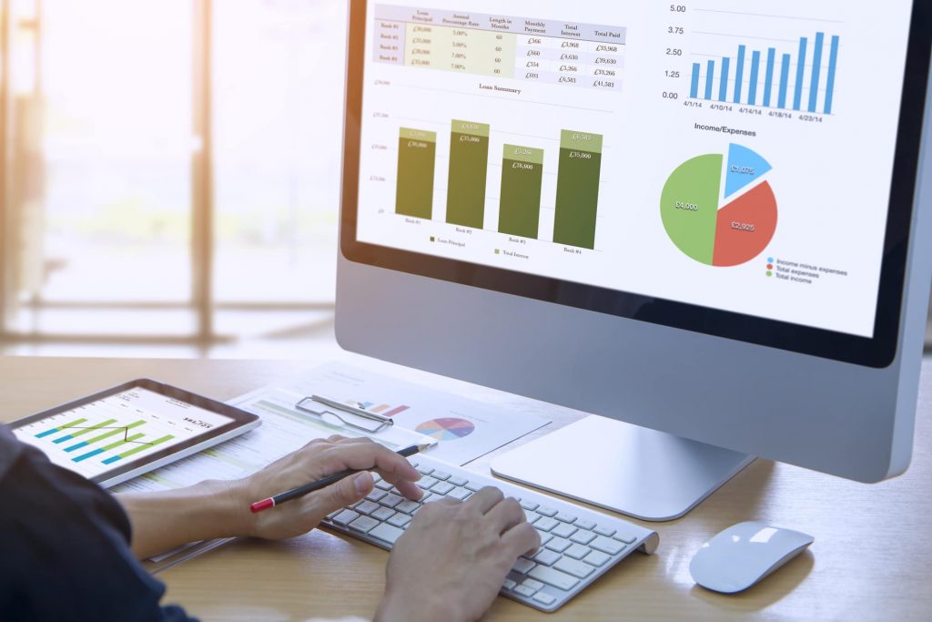 Businessman in front of modern computer with colorful pie and bar graphs analysing business performance accounting data, custom software, app development