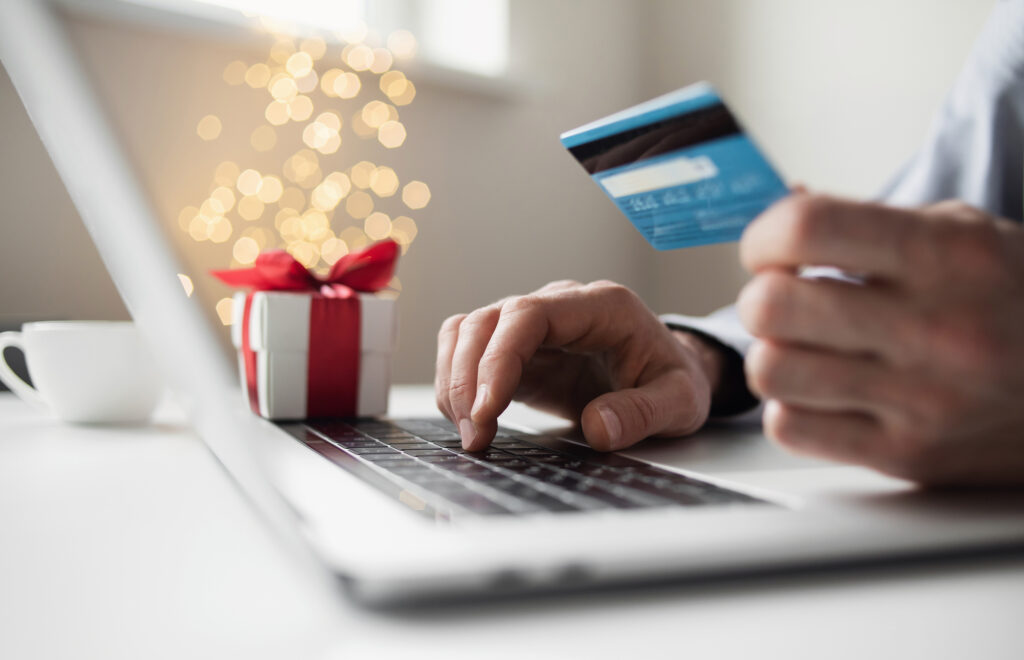 Online shopping during holidays. Man ordering Christmas gift using laptop and credit card holiday ecommerce development